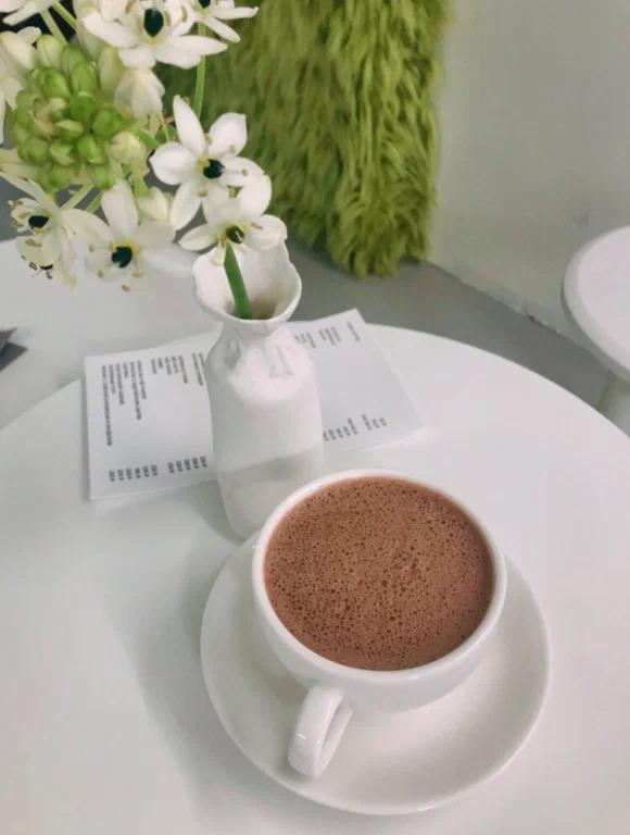 Крупный план чашки кофе на белом столе в магазине-кофейне Fjord: чашка, блюдце, маленькая ваза с цветами и минималистичная печатная карта.