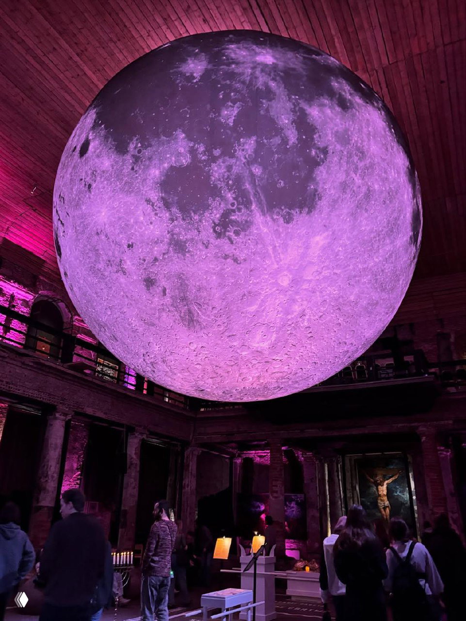 Большая сферическая инсталляция-луна в центральном зале Анненкирхе, подсвеченная розово-фиолетовым светом над посетителями и экспонатами.