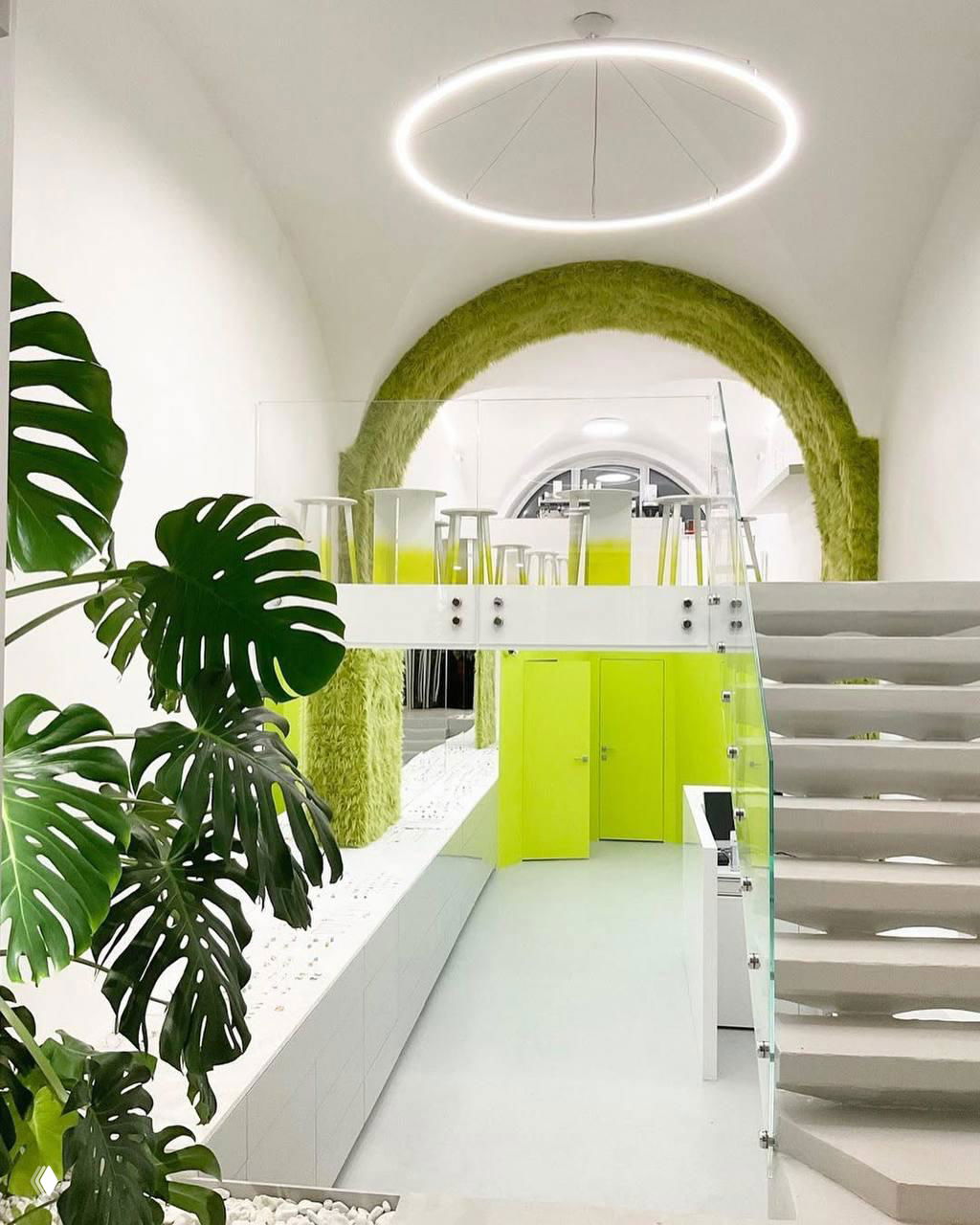 Общий вид двухуровневого пространства Fjord: лестница, стеклянные перила, зелёные арки и яркие элементы оформления на фоне белых стен.