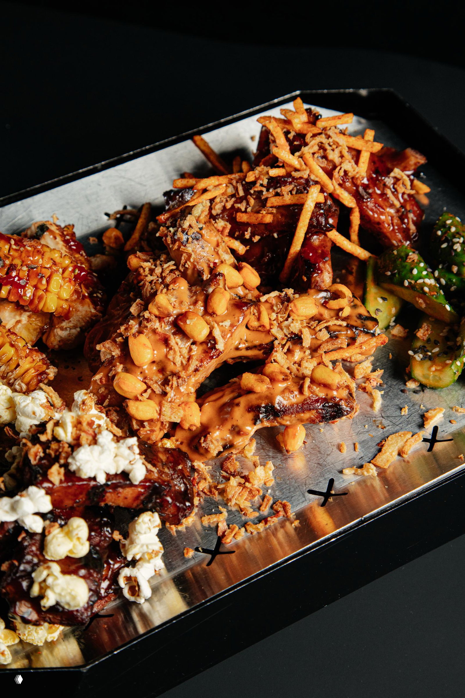 Крупный план ребёр из сета KING size VOL.3: соус, арахис, хрустящая картофельная соломка и попкорн на металлическом подносе, видны приправы и текстура