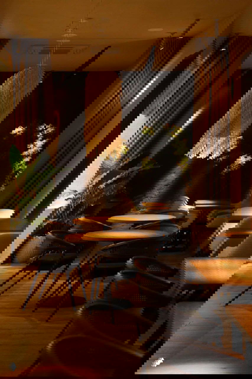 Зал ресторана с круглыми деревянными столами, плетёными креслами, макраме-абажуром и крупными растениями — минималистичный и тёплый дизайн.