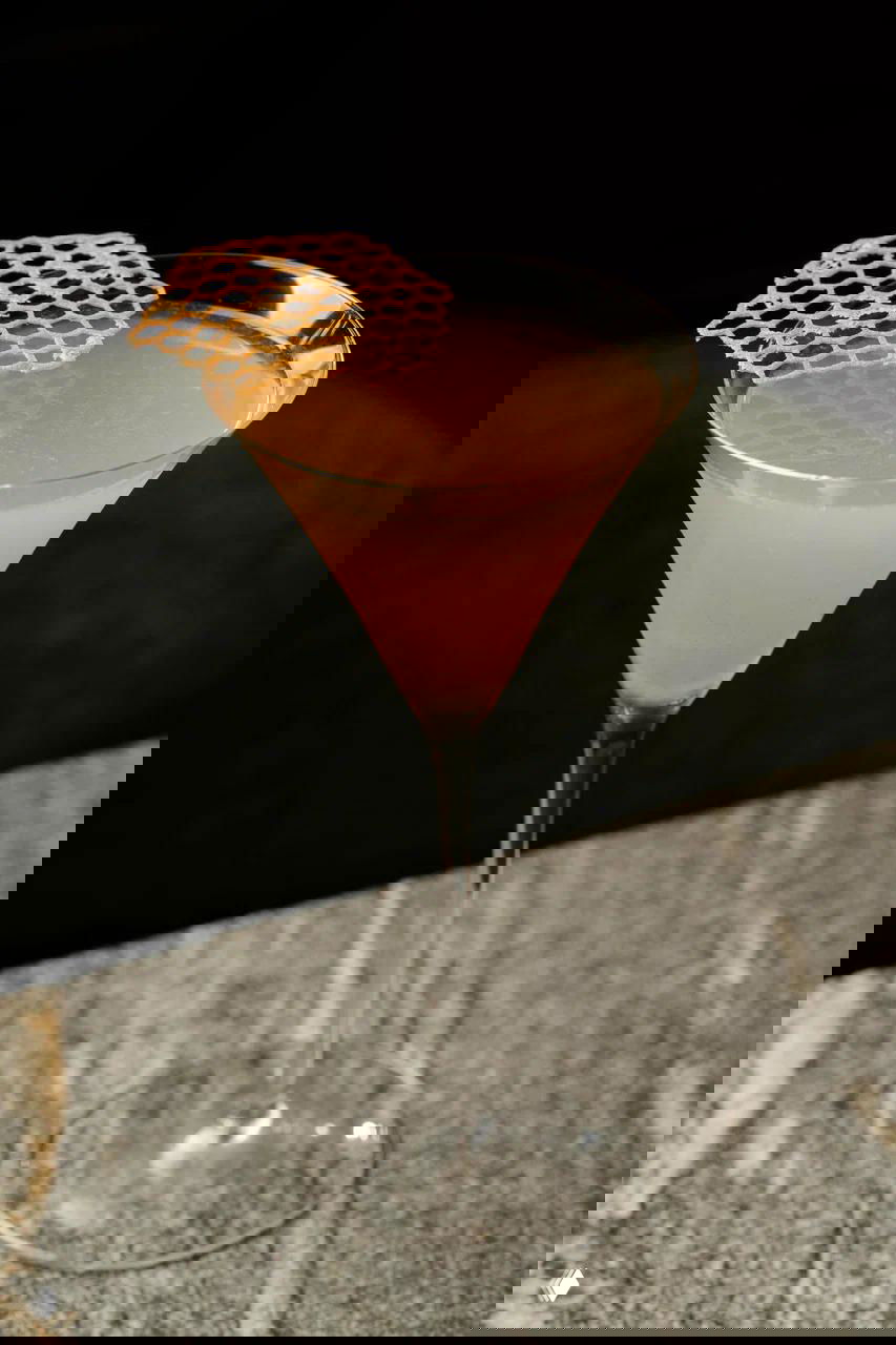 Коктейль в мартиновском бокале с ажурной хрустящей декорацией на краю — авторская подача напитка на темном фоне столешницы.