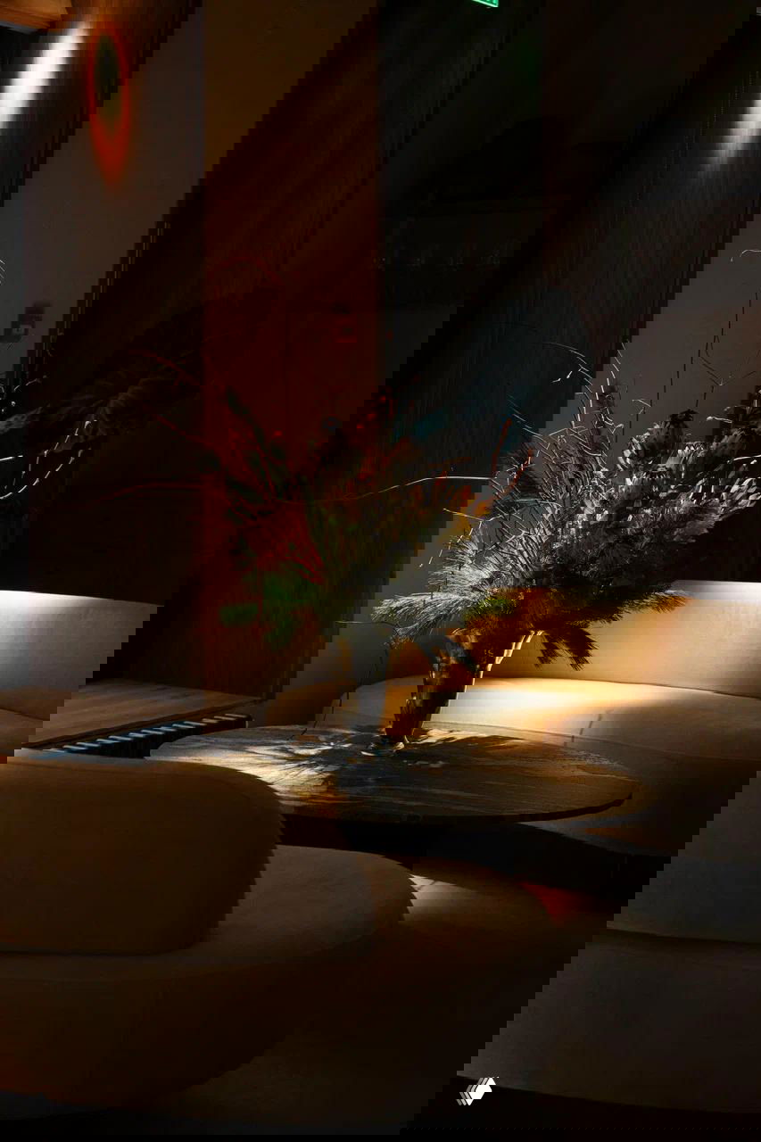 Флористическая композиция на низком круглому столе в зоне отдыха с диванами, мягким боковым светом и выразительной текстурой материалов интерьера.