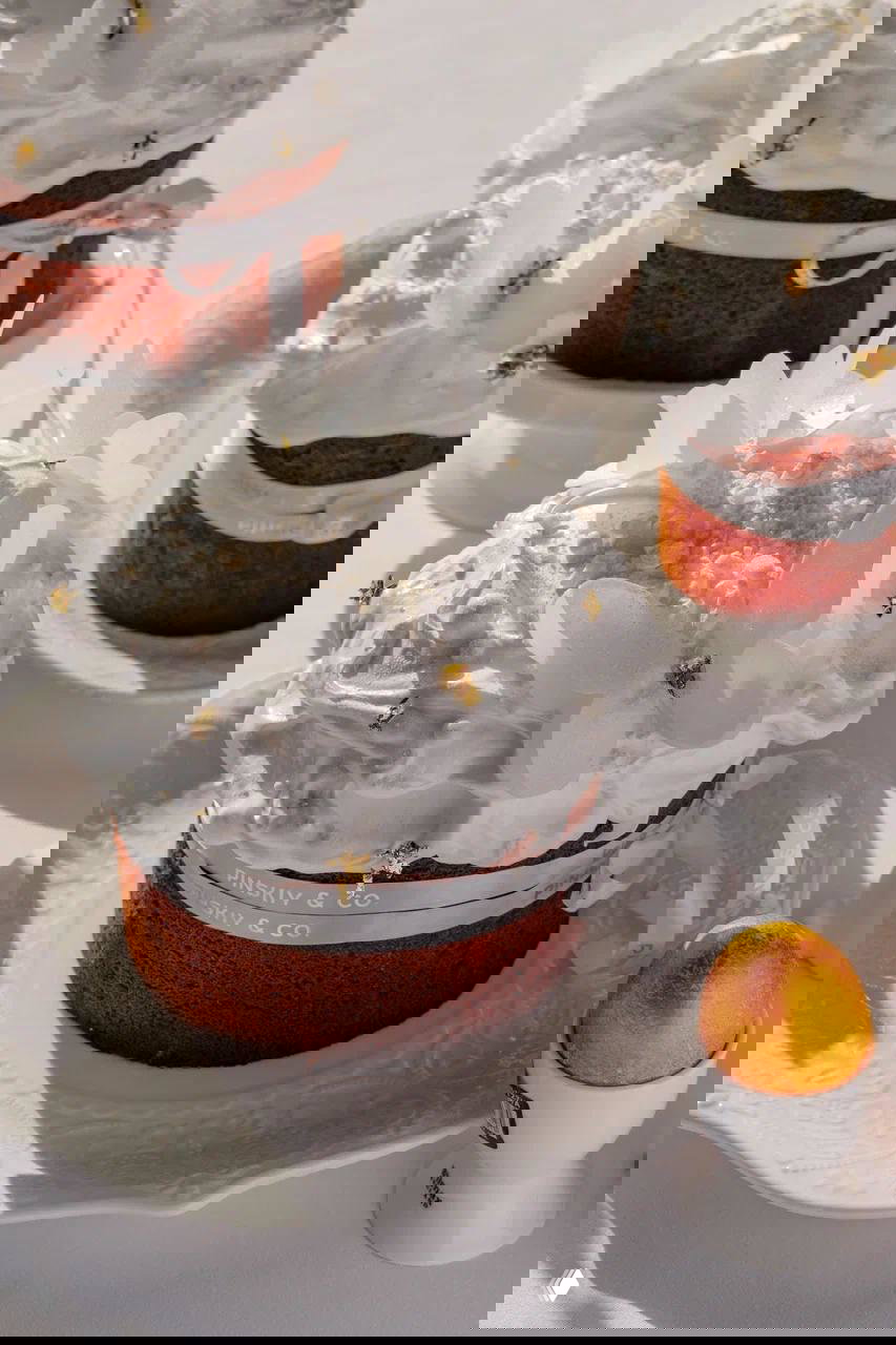 Украшенные мини-куличи панеттоне с белой безе-глазурью, бумажными бабочками и золотыми декоративными акцентами на сервировке.