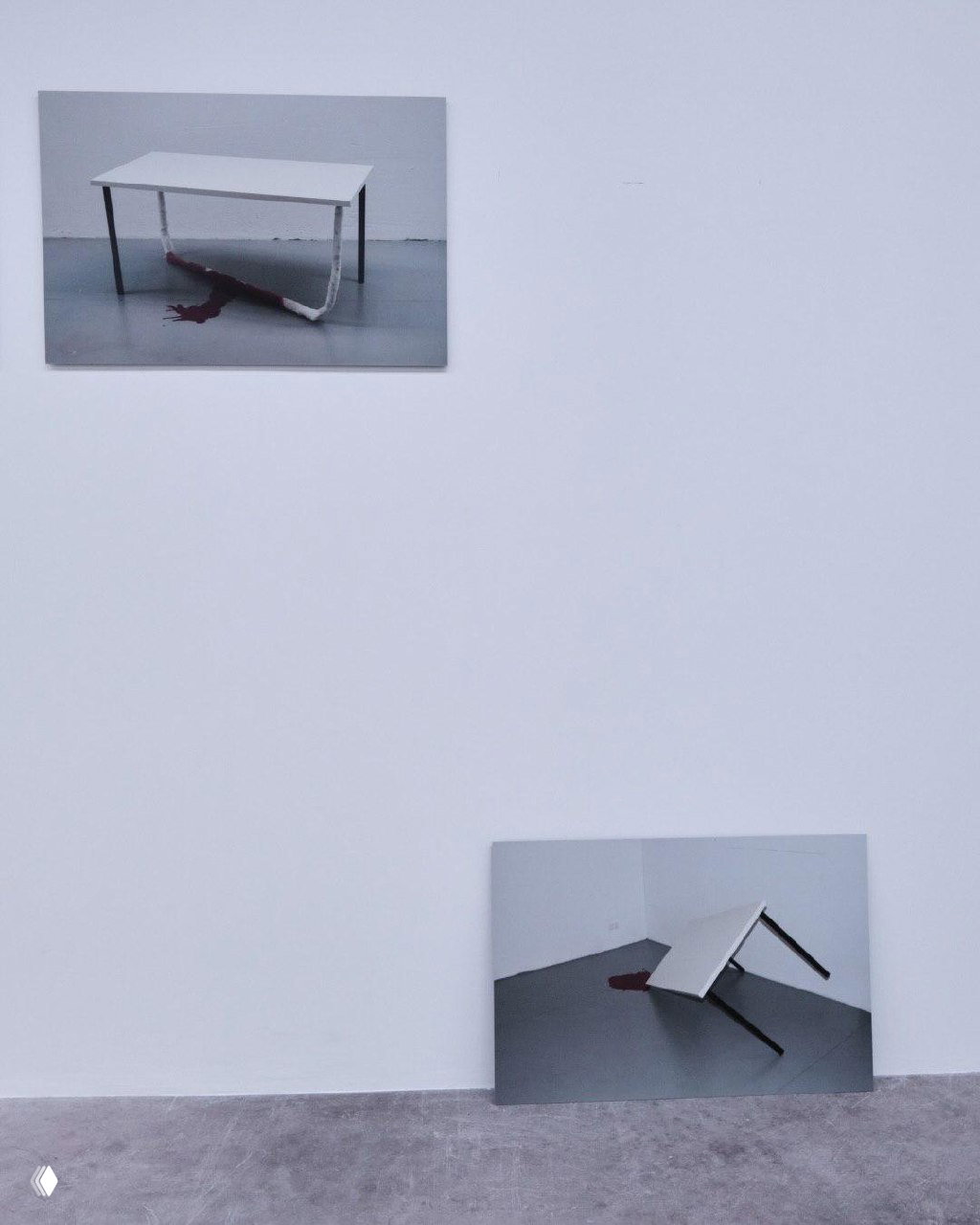 Фотографии работ Савельева: изображение белого стола с тёмным пятном на полу — фрагмент инсталляции, представленной на выставке.