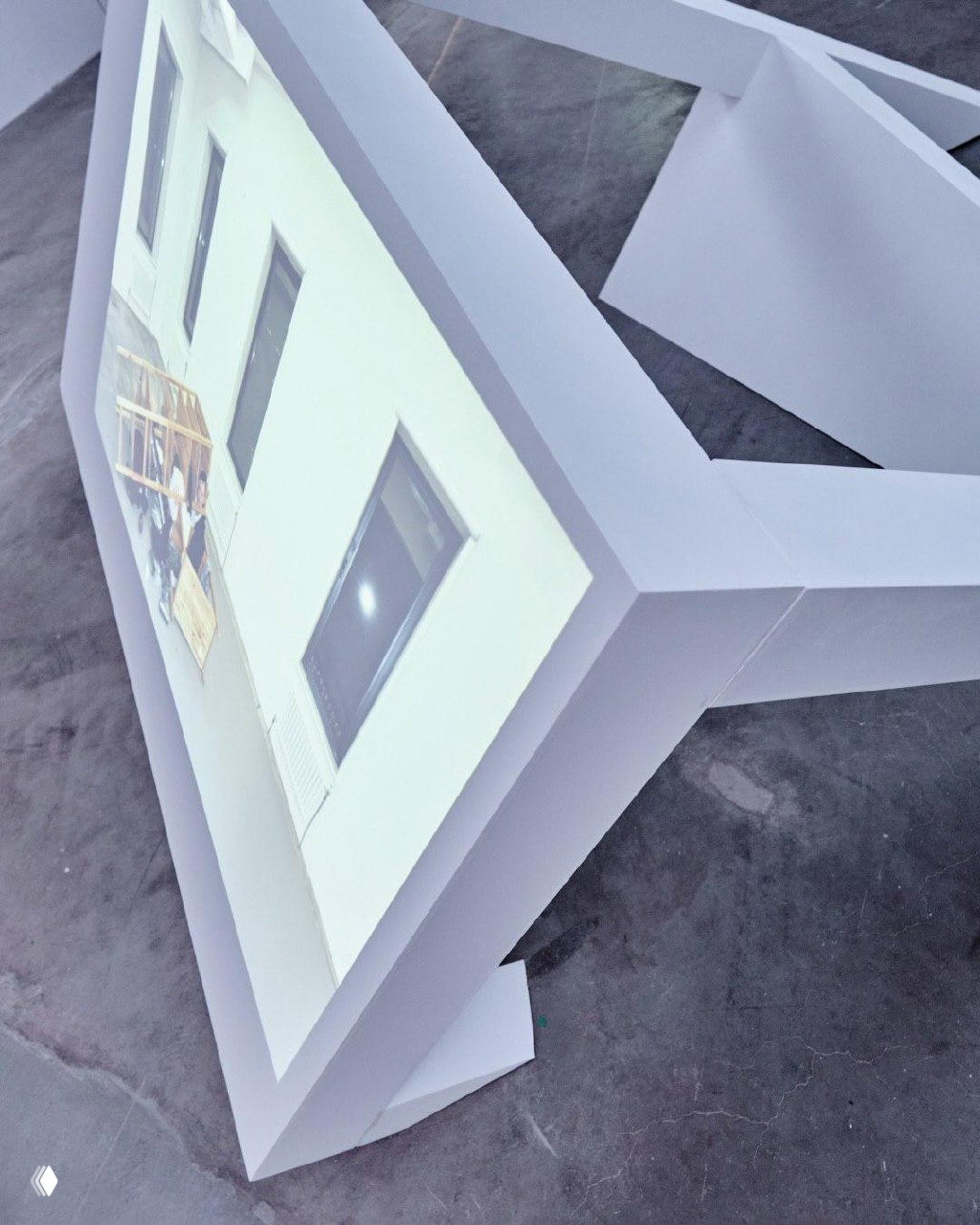 Крупный план объёмной рамной инсталляции с проекцией, видна структура корпуса и отражение окон в светлом зале галереи.