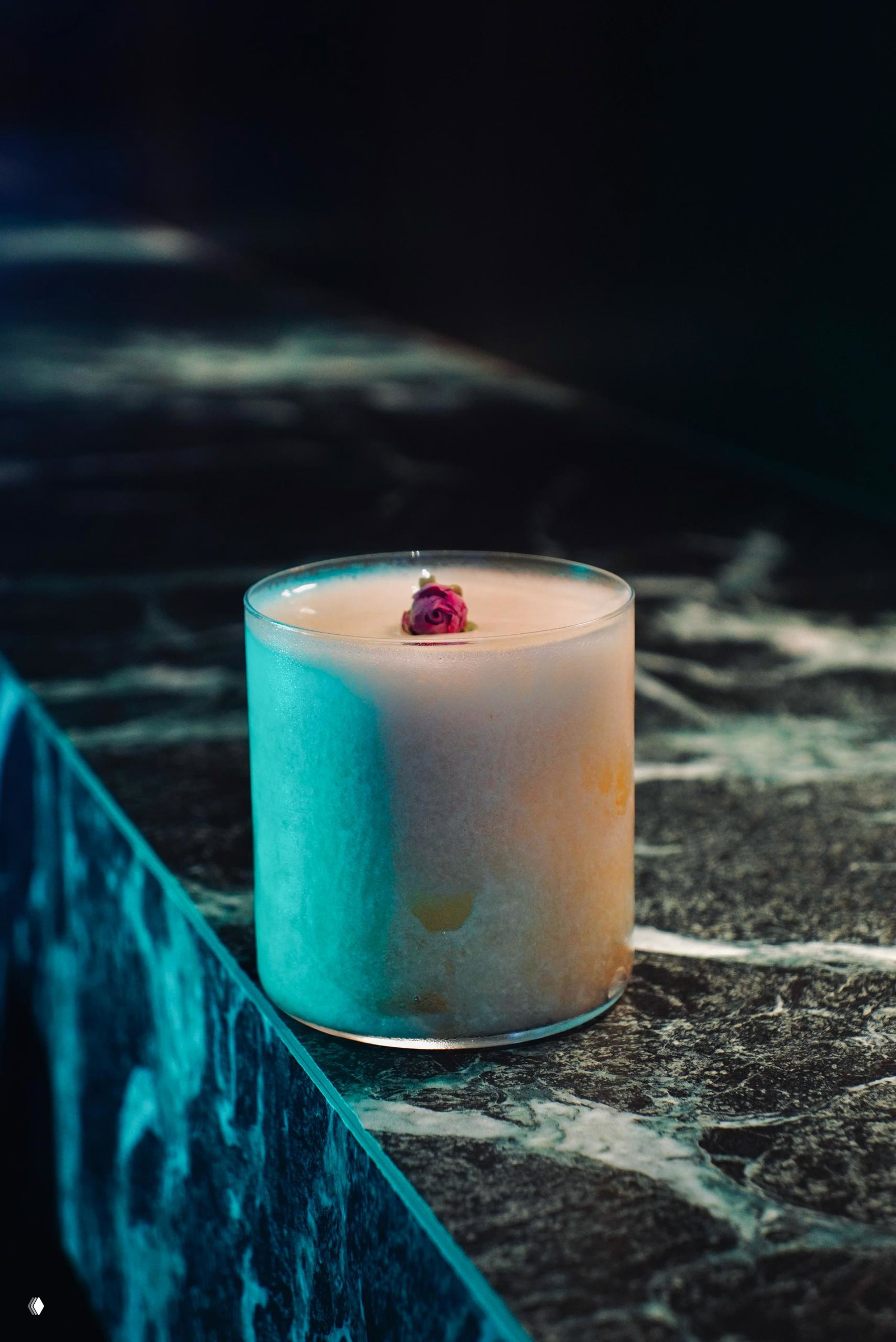 Коктейль в низком стакане с розой на пене на мраморной стойке бара Quoroom — пример подачи авторских напитков в заведении с камерной атмосферой.