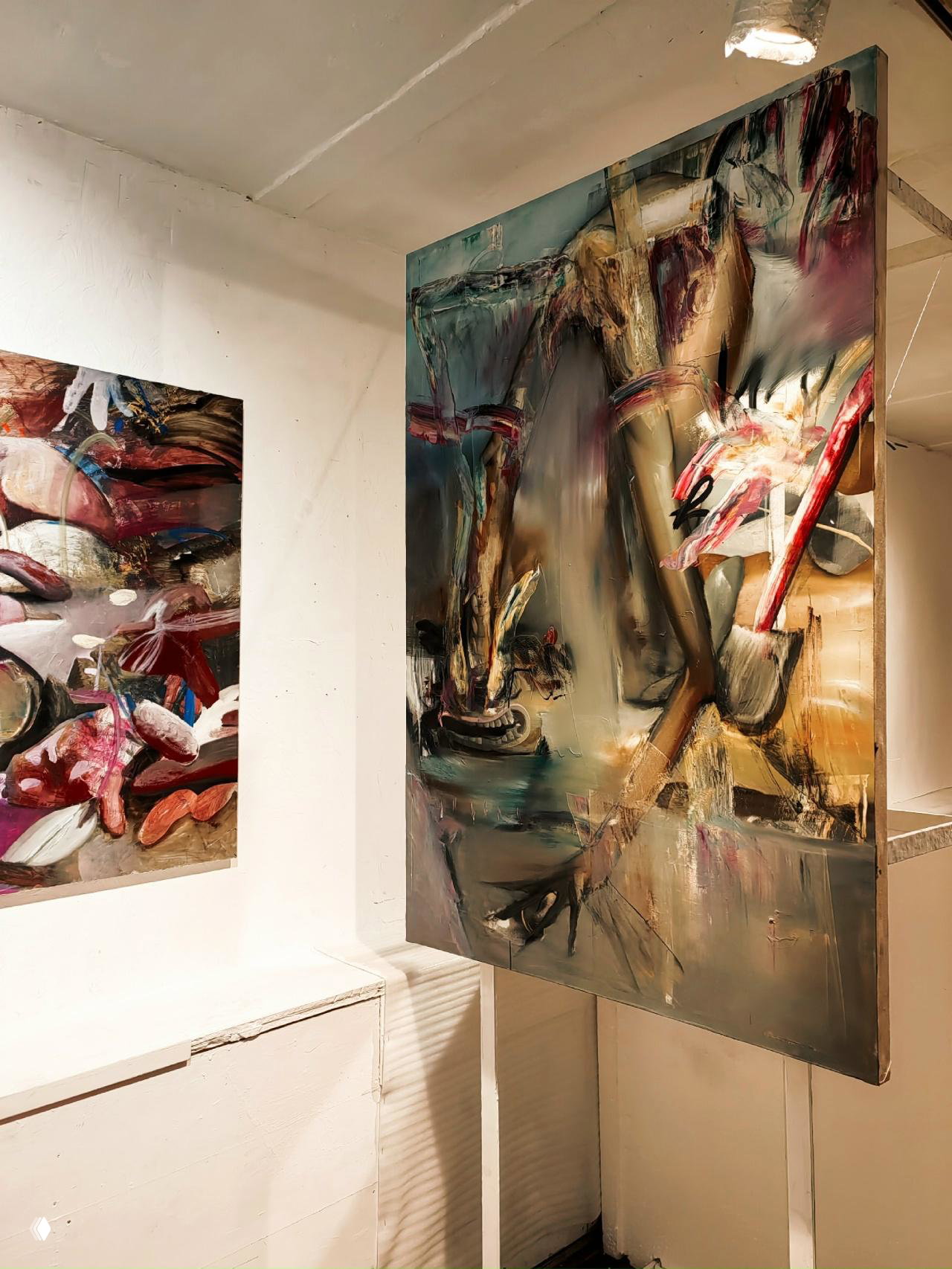 Фрагмент экспозиции: висящее большое полотно с динамичными мазками и мягкой градацией цвета, видны трещины потолка и источники света.