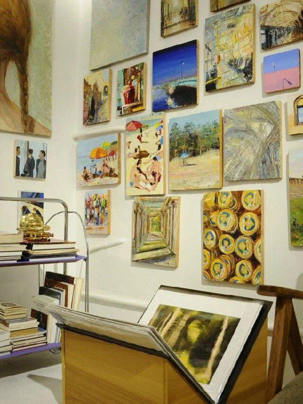 Интерьер галереи: плотная экспозиция небольших картин на стене, внизу — подставки и рамки для продажи, ощущение уютного арт-пространства.