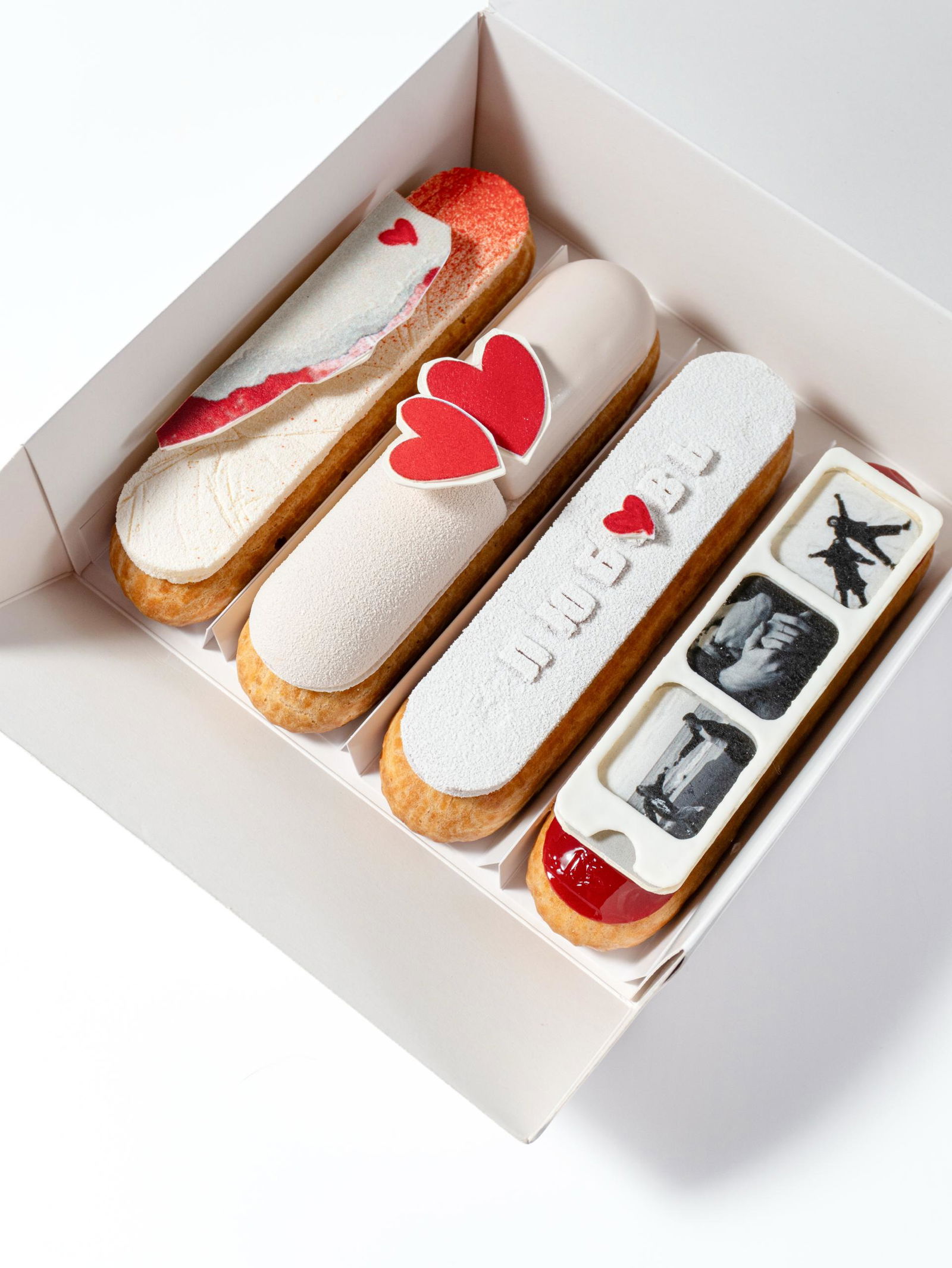 Коробка с четырьмя аккуратными эклерами в романтическом оформлении: белые и розовые глазури, съедобные сердечки — праздничный десерт резидентов рынка.