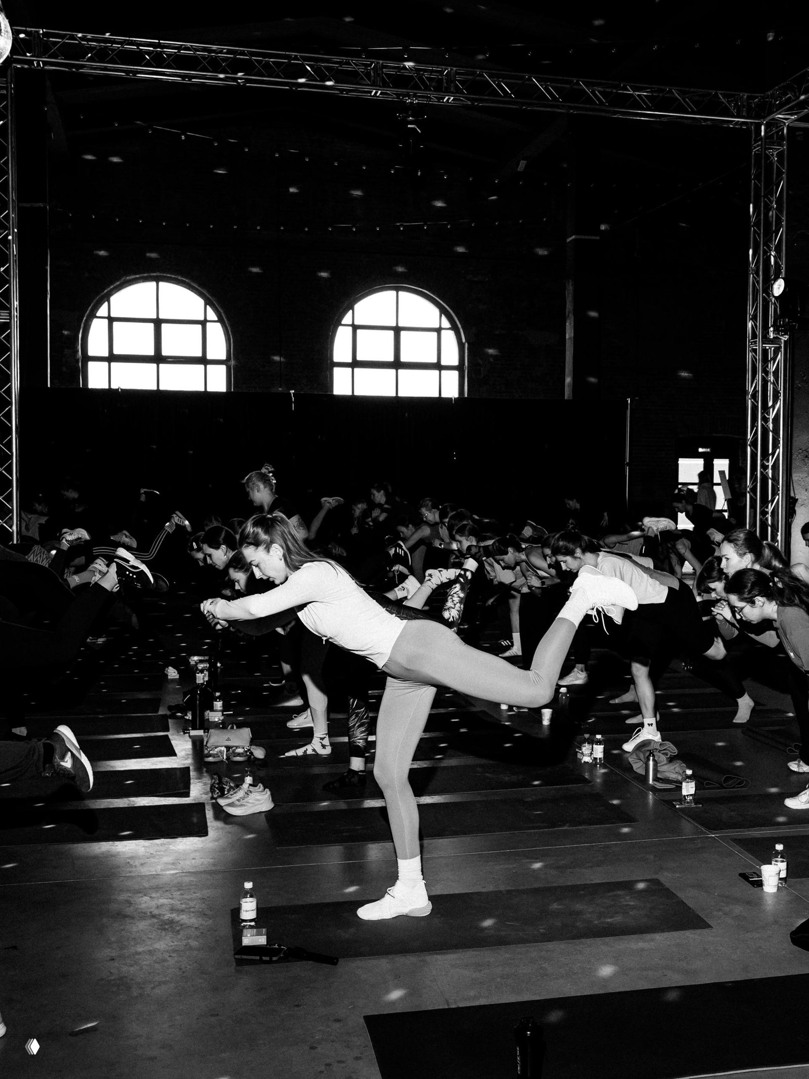 Черно‑белая сцена с участниками, выполняющими балансирующие и растяжечные движения во время массовой фит‑сессии.