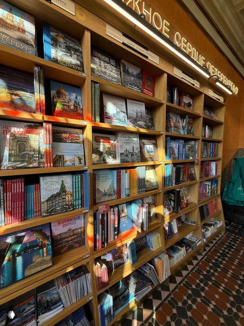 Полки книжного магазина с туристическими и краеведческими книгами, солнечные блики на обложках и мраморная плитка на полу — интерьер Дом Книги.