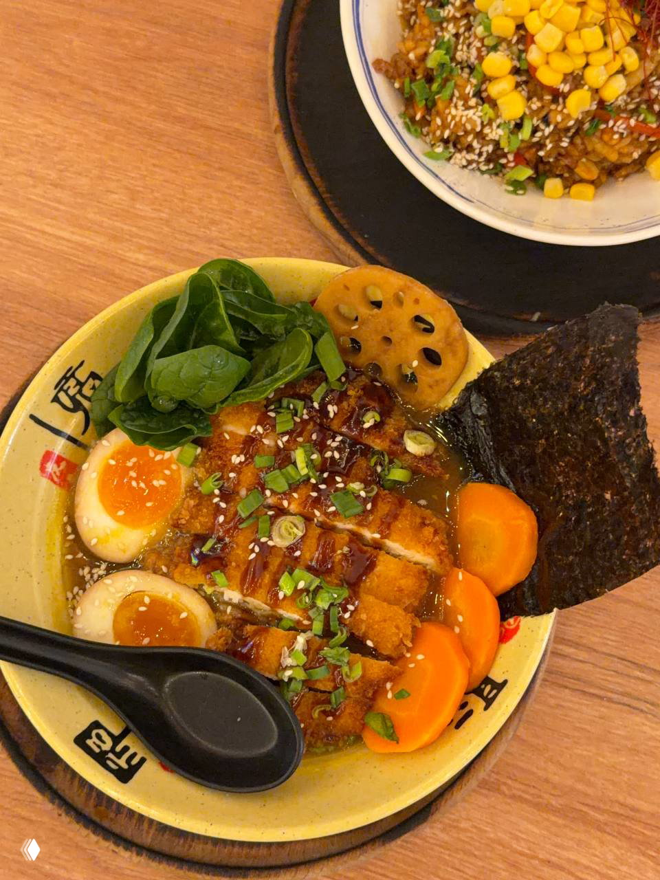 Крупный план карри рамэна с курицей кацу: варёное яйцо, листы шпината, морковь, ломтики кatsu и лист нори на миске с бульоном.