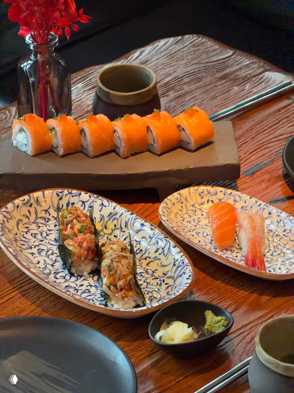 Тарелки с роллами и сашими на деревянном столе: Ролл Филадельфия лосось и суши лосось рядом с васаби и маринованным имбирём, сервировка в азиатском стиле.