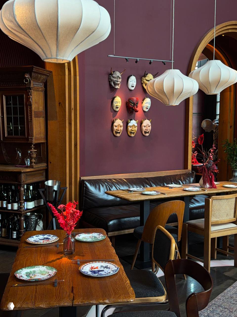 Интерьер ресторана с декоративными японскими масками на стене, мягкими лампами и столиками у дивана — сочетание китайско-японской эстетики и винтажных деталей.