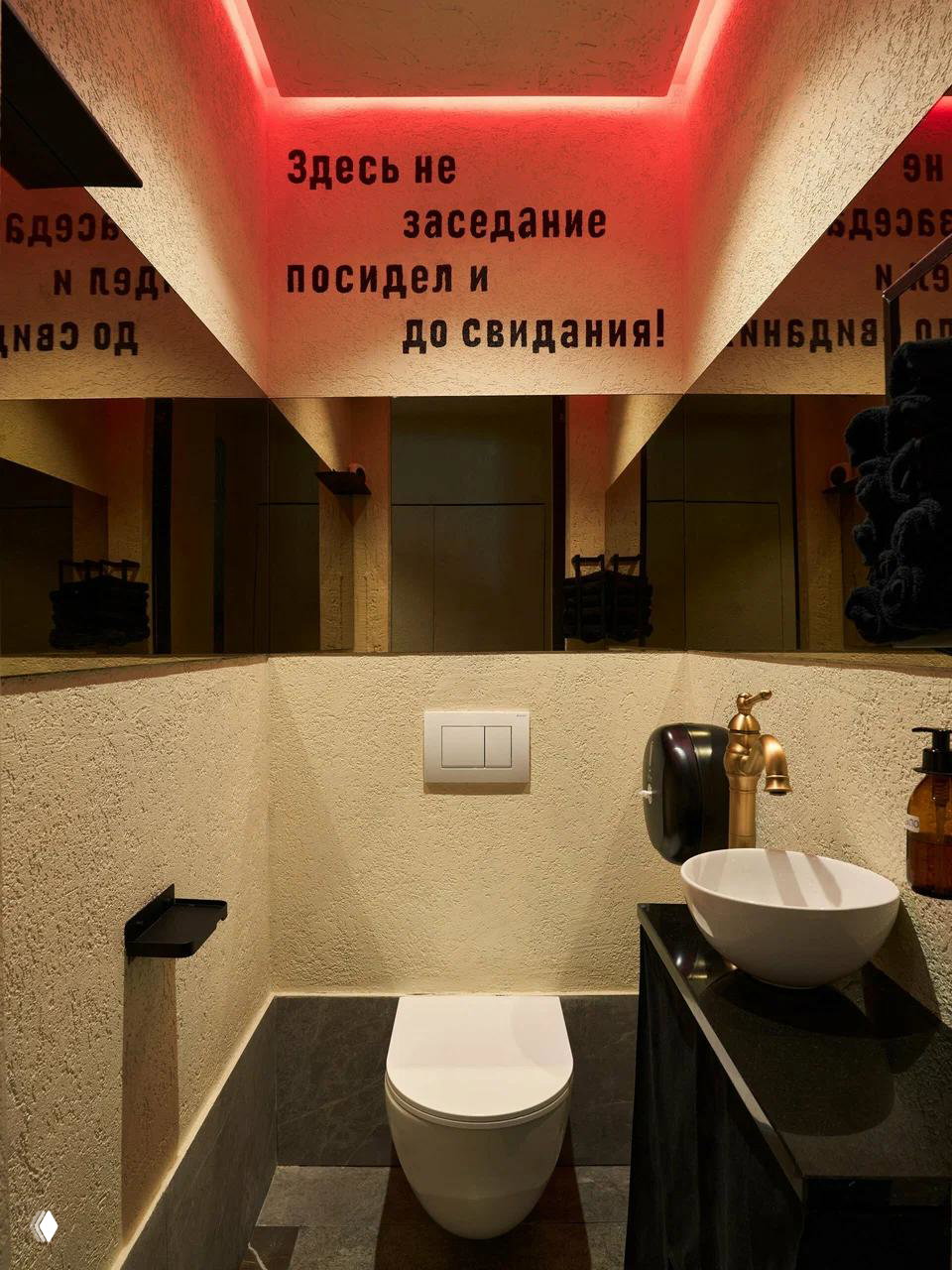 Интерьер туалета заведения: компактая комната с зеркалами, золотистым краном и надписью на потолке «Здесь не заседание посидел и до свидания!».