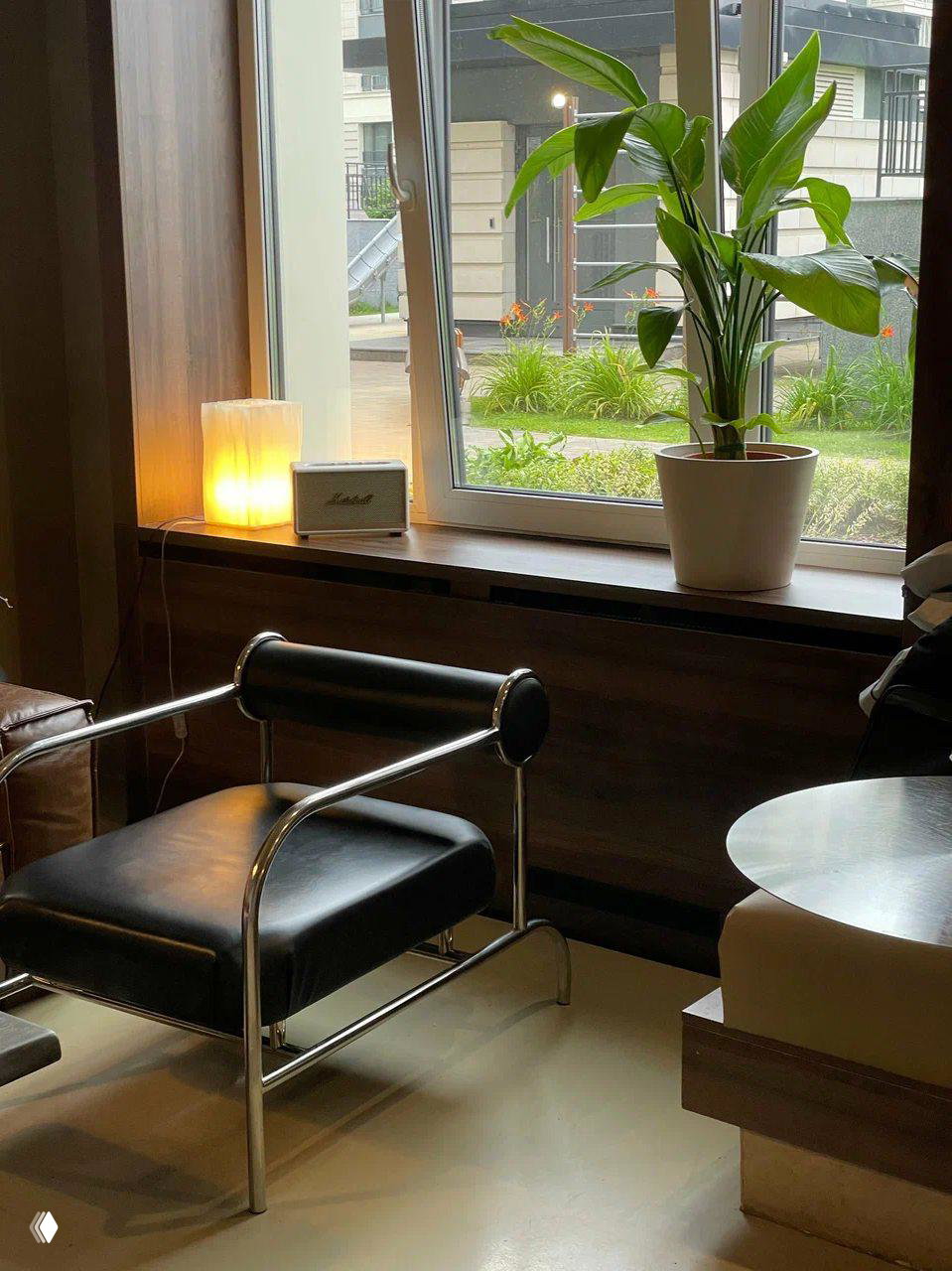 Уголок кофейни с кожаным креслом, лампой на подоконнике и зелёным растением — спокойная зона для просмотра фильмов и отдыха.