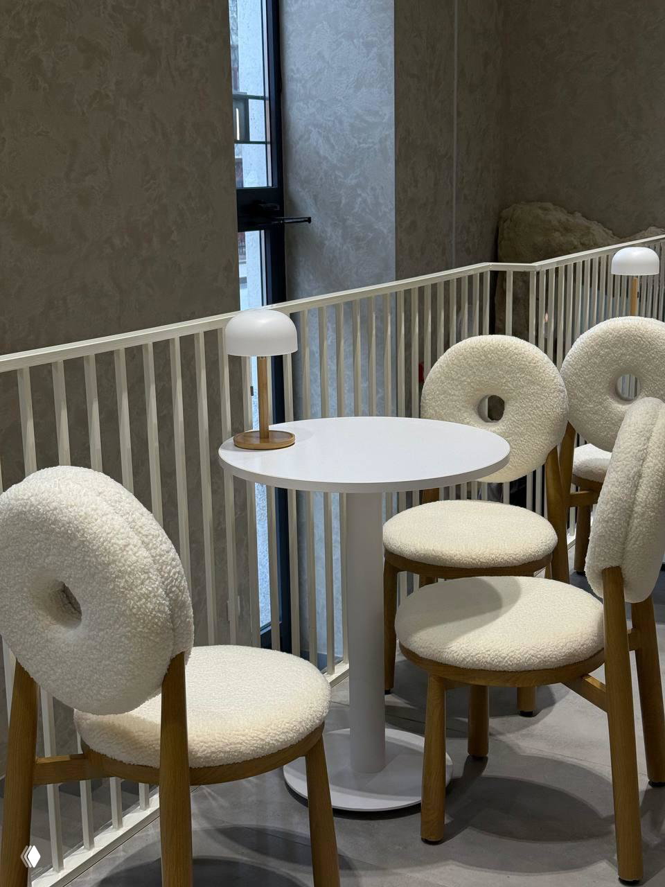 Второй уровень кафе с белыми круглых сиденьями с отверстием в спинке, небольшими столиками у перил и настольными лампами — светлая зона для гостей.