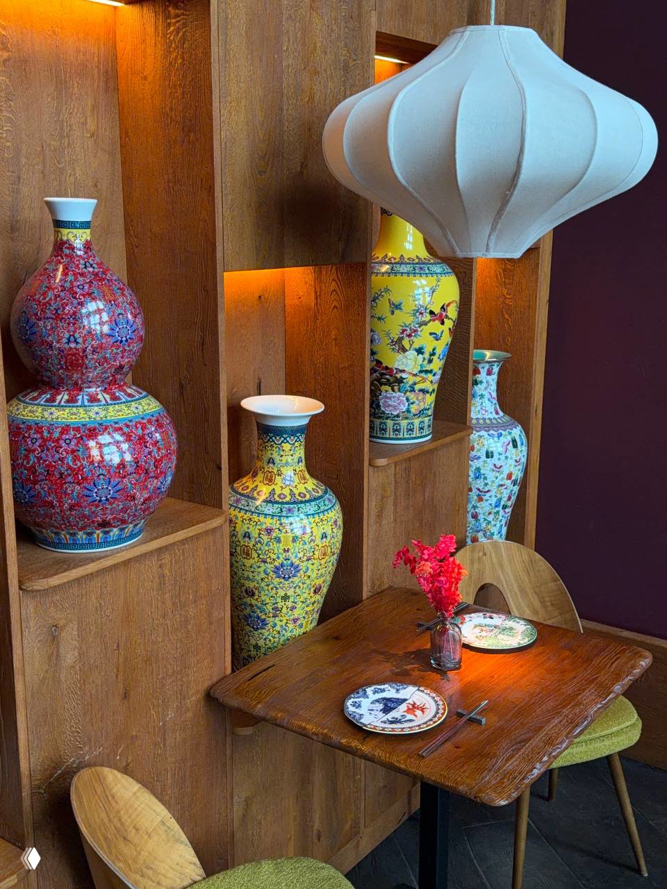 Уголок ресторана с деревянной витриной и высокими расписными ваза-изделиями, маленький столик на двоих и кресла — элементы декора в китайском стиле.