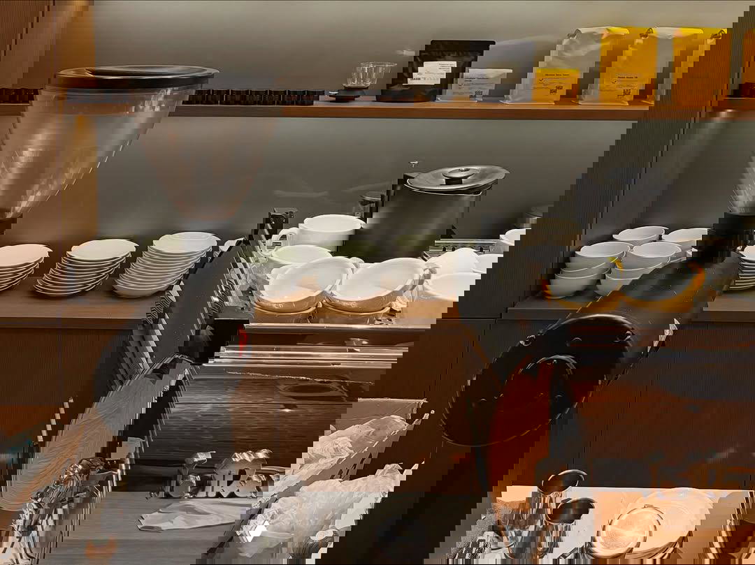 Рабочая кофейная станция в поп-ап «Смена»: крупная кофемолка, эспрессо-машина, стопки чашек и упаковки кофе на полке за баристой.