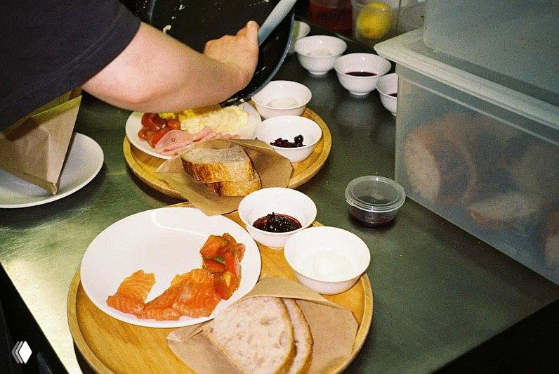 Подносы со завтраком: хлеб, копчёная семга, небольшие миски с соусами и ингредиентами — вид на процесс подготовки блюд в кухне.