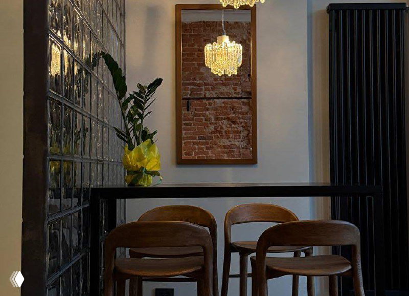 Уютный уголок с барной стойкой, деревянными стульями, зеркалом и кирпичной стеной — интерьер поп-ап кофейни «Смена» оформлен в тёплых тонах.