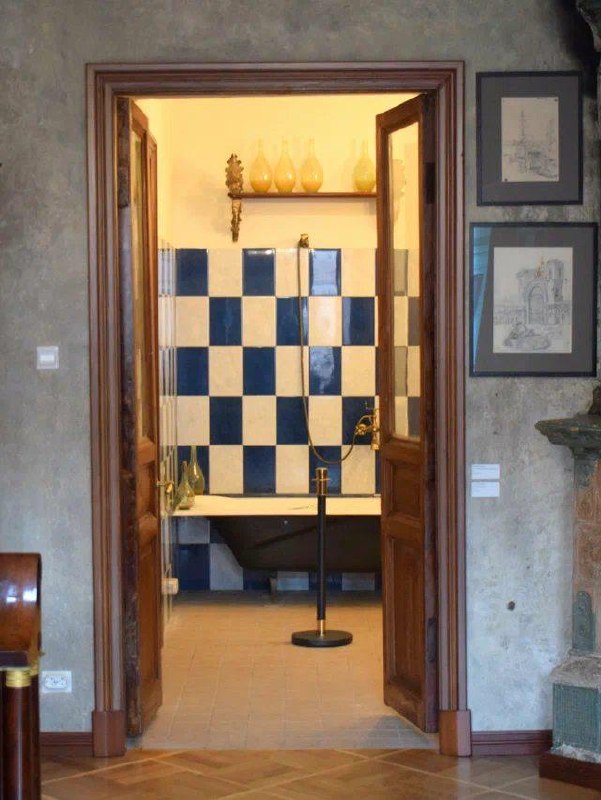 Вид через дверной проём на музейную ванную с сине‑белой шахматной плиткой и чёрной ванной — часть воссозданного интерьера квартиры.