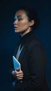 Портретная фотография женщины в строгом костюме с планшетом в руках, возможно организатор или судья конкурса, напряжённый взгляд в сторону.