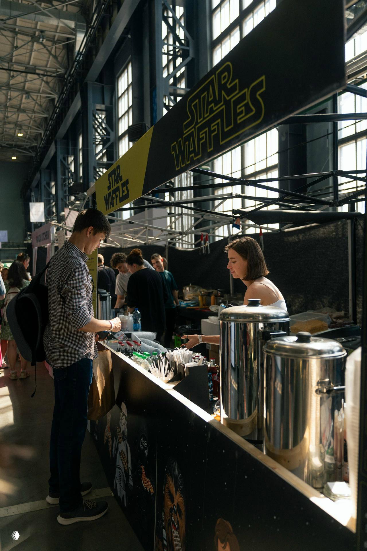 Фуд-корнер с вывеской «Star Waffles»: продавцы и посетители у прилавка с чайниками и стаканчиками на фуд-маркете фестиваля.
