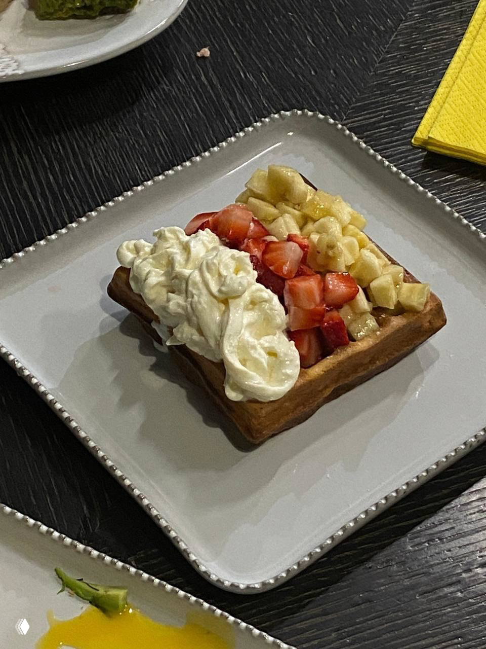 Крупный план венской вафли на квадратной тарелке: порезанные клубника и банан, щедрая порция взбитых сливок на тёмном столе — деталь меню «Секретера».