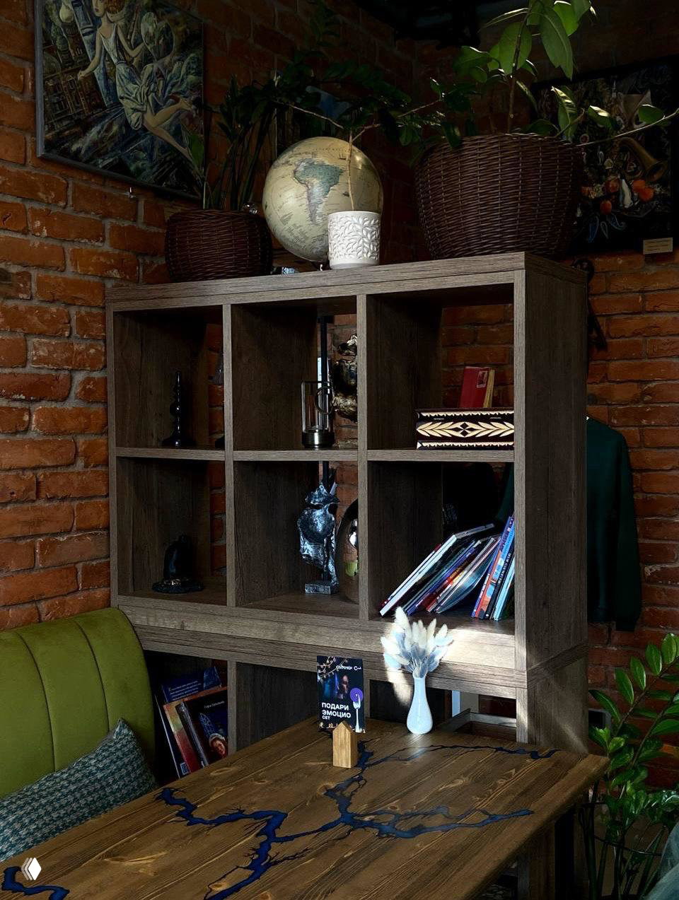 Деревянная полка-стеллаж с глобусом, книгами и растениями на фоне кирпичной стены — уголок собственной библиотеки в кофейне «Секретер».