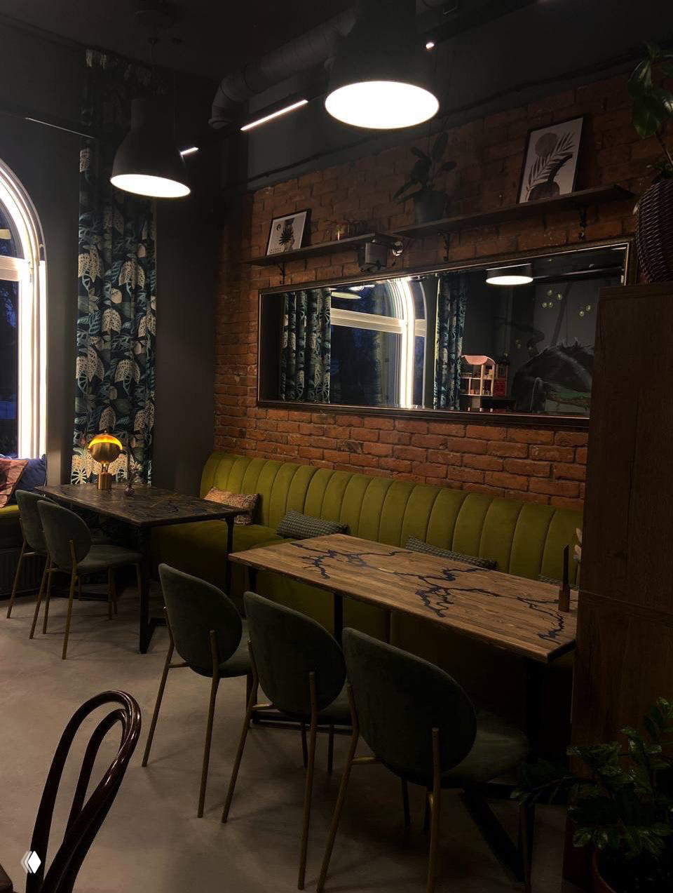 Широкий вид зала: зелёная длинная лавка, зеркальная панель и несколько столов под промышленными светильниками — стильный интерьер для встреч и мероприятий.