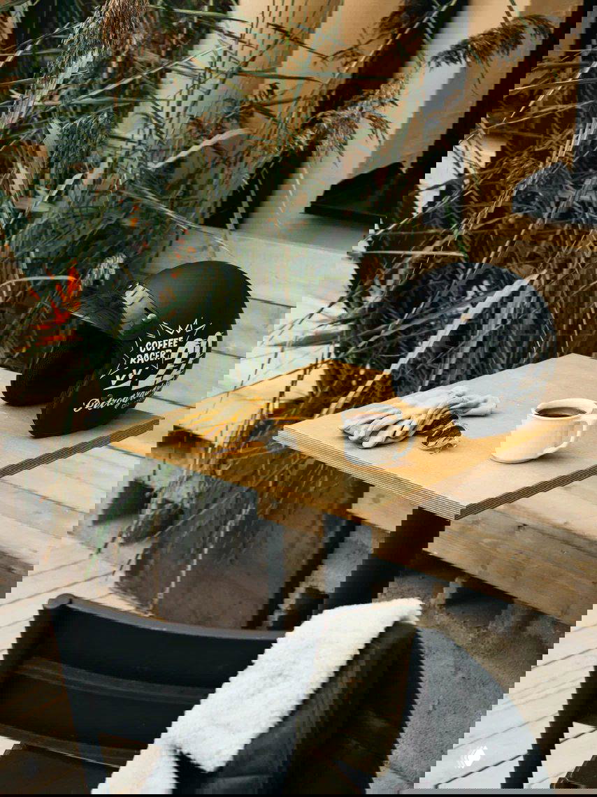 Небольшой уличный стол на террасе с кружкой кофе, перчатками и шлемом с надписью «Coffee Racer» — уютная кофейная зона на свежем воздухе.