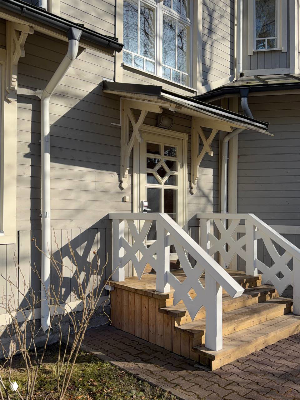 Декоративный вход с белой резной перилой и деревянными ступенями у коттеджа на территории клуба «Скандинавия», солнечный день и аккуратный подъезд.