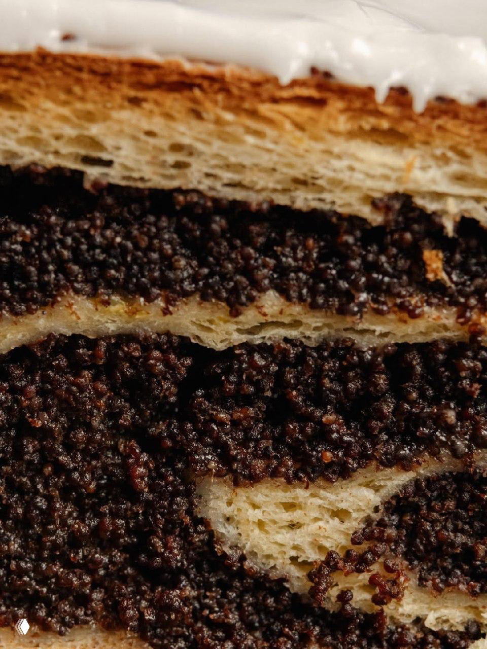 Крупный план разреза булки с плотной маковой начинкой и слоем белой глазури — текстура теста и маковая прослойка видны детально.