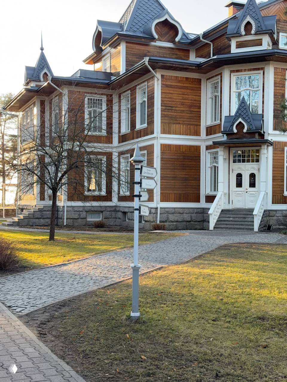 Деревянный особняк в стиле дачи Лихачева на территории клуба «Скандинавия», каменная подложка, дорожки и указатель направлений у входа в главный дом.