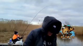 Кадр из видеопревью: рыбак на переднем плане и второй на берегу с удочкой у камыша во время ловли.