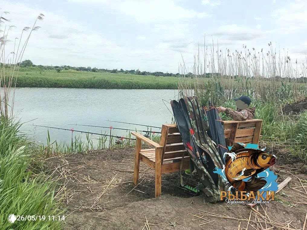 Берег пруда «У ГАФУРА» с лавочкой, несколькими удочками на подставках у тростника, спокойная вода и фирменный логотип канала.