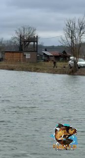 Прибрежная зона с деревянной постройкой и человеком вдалеке на фоне Серебряных прудов; облачное небо и растительность вдоль берега.