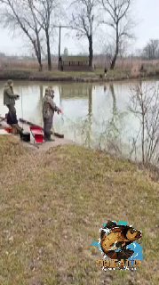 Краткий кадр с рыбаками на деревянном причале у пруда: двое с удочками и сумками, вокруг тихая водная гладь и лодки.