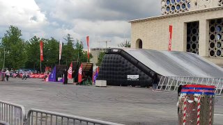 Площадка спортивного праздника в Лужниках: надувная трасса и сцена на открытой площади, ограждения и первые ряды зрителей на фоне зданий.