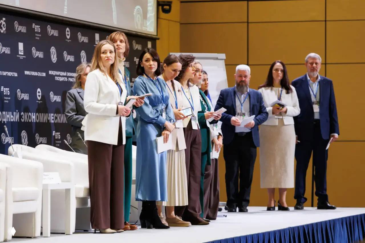 Группа участников и спикеров на сцене форума в деловой одежде, подготовка к панельной дискуссии и обмен материалами между участниками.