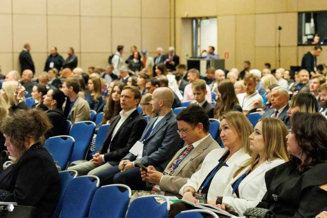 Публика в зале конференции: слушатели на креслах, деловые беседы в перерывах и внимание к выступлениям на сцене большого форума.
