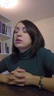 Женщина-лектор в домашней студии во время записи эфира: крупный план, видна полка с книгами и светлая стена на заднем плане.