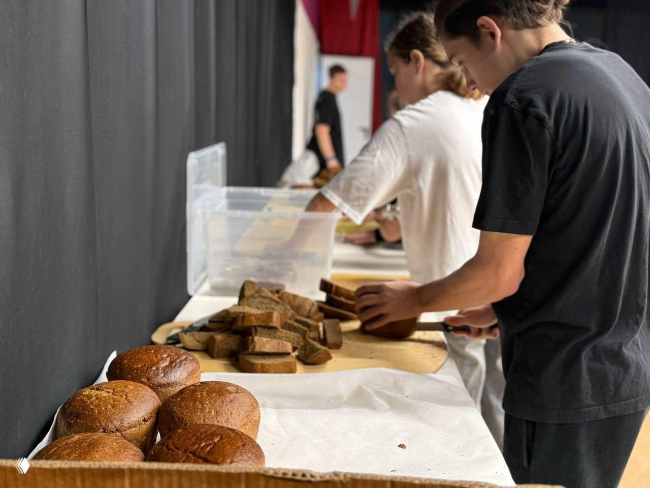 Стол с буханками и ломтями хлеба, люди режут и раздают хлеб — символические талоны и сценическая реплика блокады.