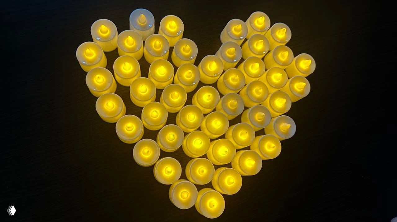 Множество небольших светодиодных свечей, выложенных в форме сердца на тёмной поверхности — символ уюта, поддержки и безопасного пространства группы.