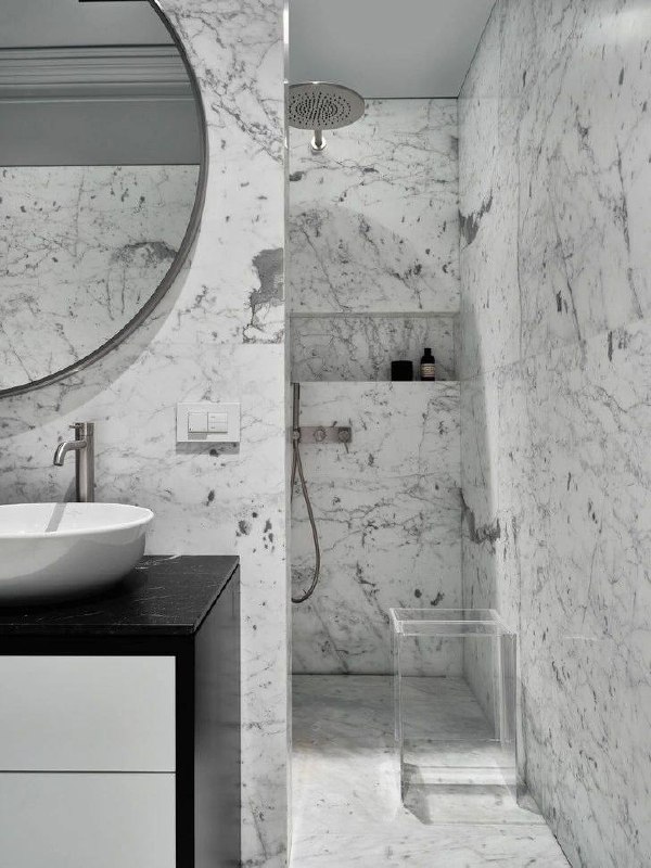 Ванная комната отделана белым мрамором: душевая ниша, настенная мраморная отделка и минималистичная сантехника в лаконичном стиле.
