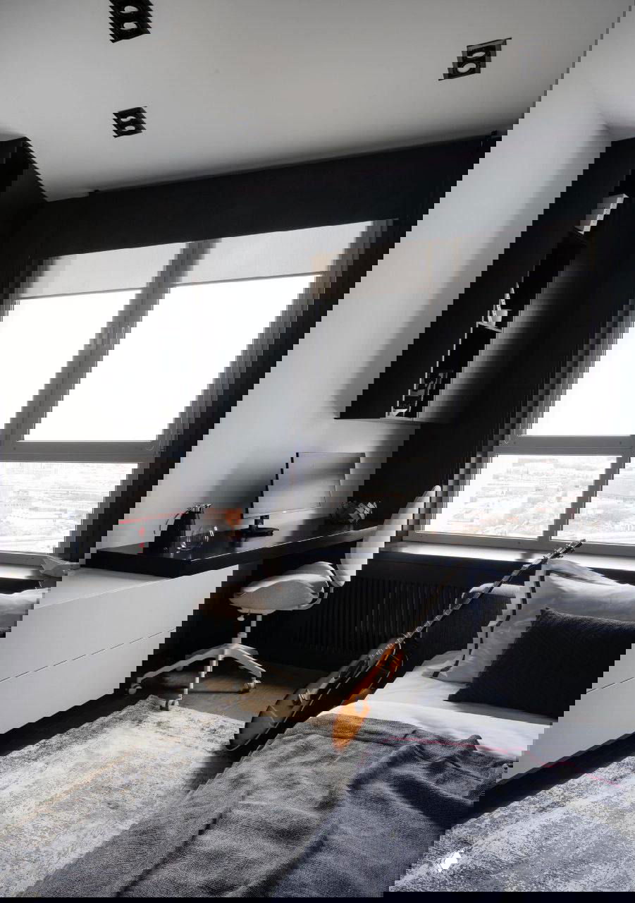 Маленькая гостиная/спальная зона у тёмной фактурной стены: серый диван-кровать, декоративные подушки и навесные светильники создают контраст и текстуру интерьера.