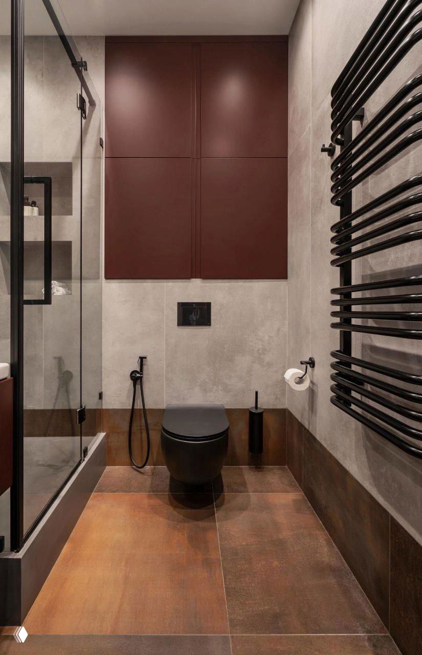 Компактная ванная комната с душевой кабиной, раковиной и мебелью винного цвета; тёплая напольная плитка и тёмные элементы сантехники в кадре.
