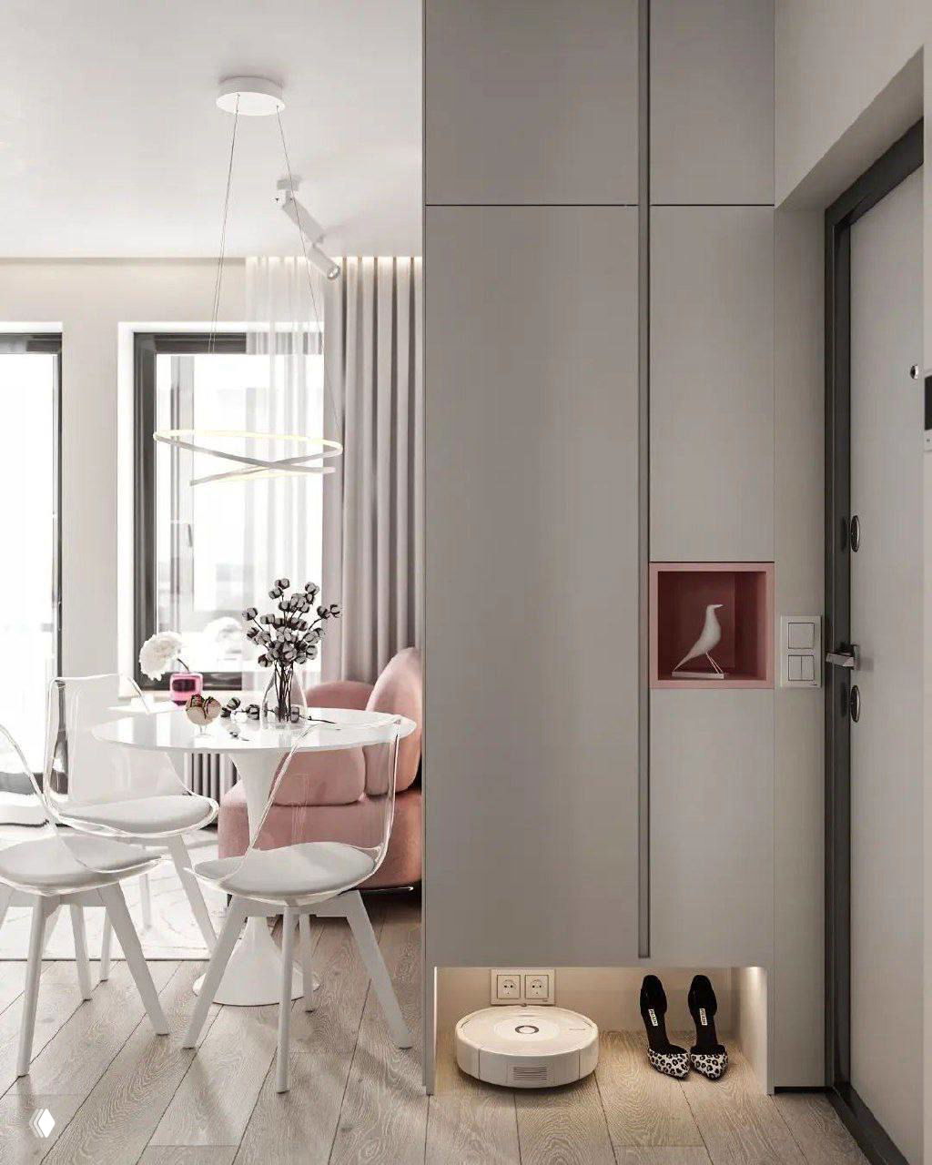 Прихожая и зона у входа в однушке: высокие встроенные шкафы, ниша для декора, система подсветки у пола и компактный робот-пылесос на зарядке.